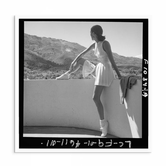 1940s vintage Toni Frissell black and white photo print of a poised model wearing a tennis-inspired outfit, elegantly perched on a ledge, gazing into the distance.
