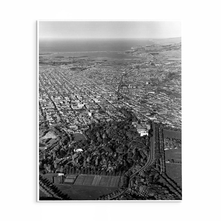 1950s black and white aerial photo of Christchurch city showing grid streets, green parks, and the bay.