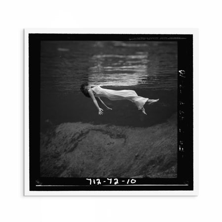 1940s black and white fashion photograph by Toni Frissell showing a woman floating in water with her dress flowing around her, evoking elegance and calm.