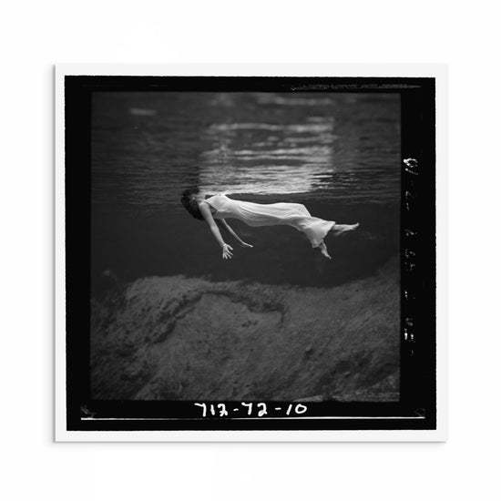 1940s black and white fashion photograph by Toni Frissell showing a woman floating in water with her dress flowing around her, evoking elegance and calm.