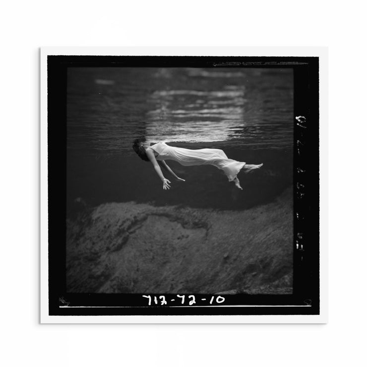 1940s black and white fashion photograph by Toni Frissell showing a woman floating in water with her dress flowing around her, evoking elegance and calm.