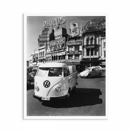 Black-and-white photograph of a VW Kombi ute and Beetle at Coca-Cola Corner, Kings Cross, Sydney, with the famous Coca-Cola sign illuminated in the background.