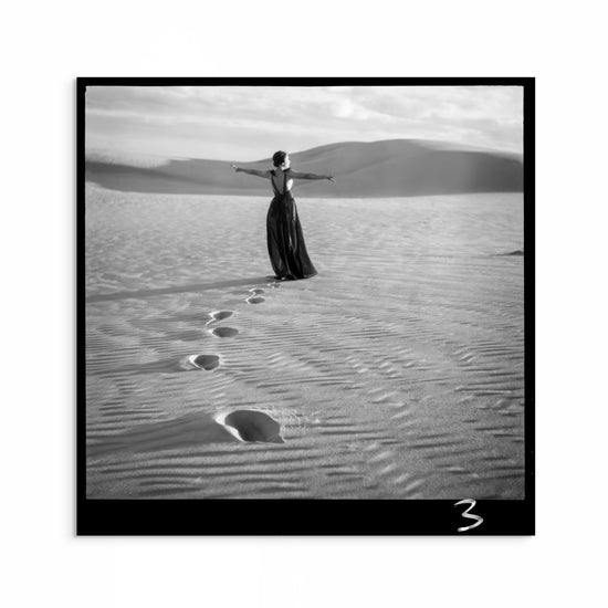 Black and white 1950s fashion photograph of a woman walking on sand dunes in a flowing gown, arms outstretched, captured by Max Dupain.
